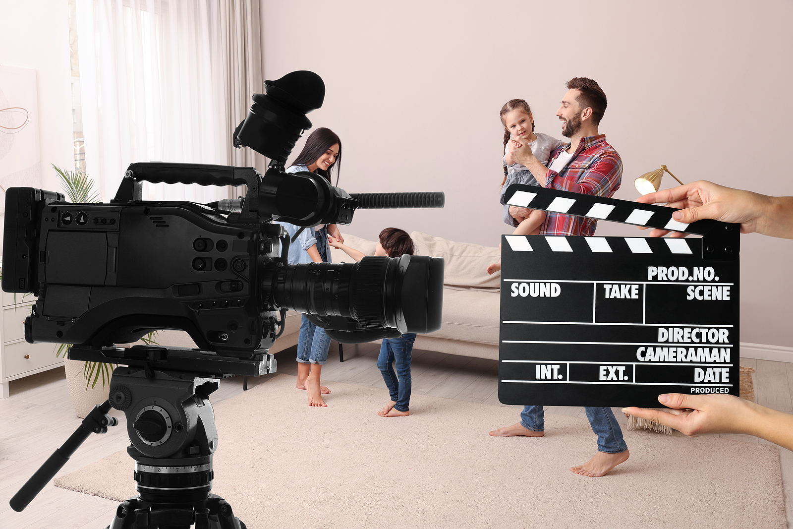 Shooting movie. Second assistant camera holding clapperboard near video camera in front of happy family (actors) at home (film set)